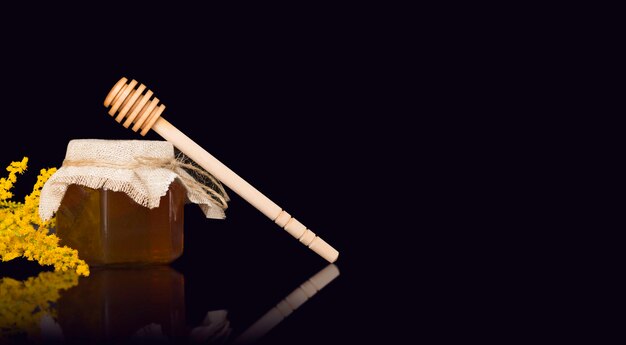 Bienenhonig in einem Glas mit Sackleinen, einem Holzspatel und gelben Blumen