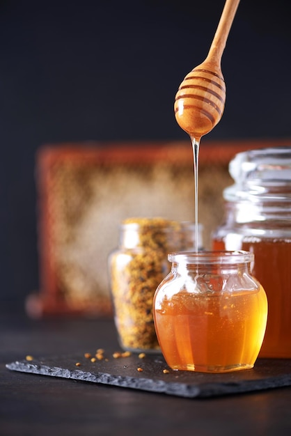 Bienenpollen-Granulat-Honigglas mit hölzerner Tropfwabe auf dunklem Hintergrund Kopierbereich Konzept der Herbsternte