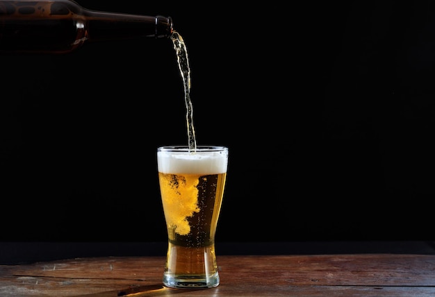 Bier in ein Glas auf einem dunklen Hintergrund des Holztischs gießen