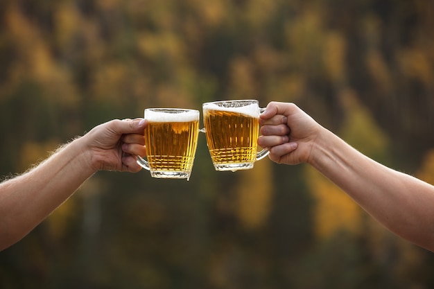 Bier in Gläsern groß und Glas hell Golden mit Schaum und Händen von Freunden Nahaufnahme