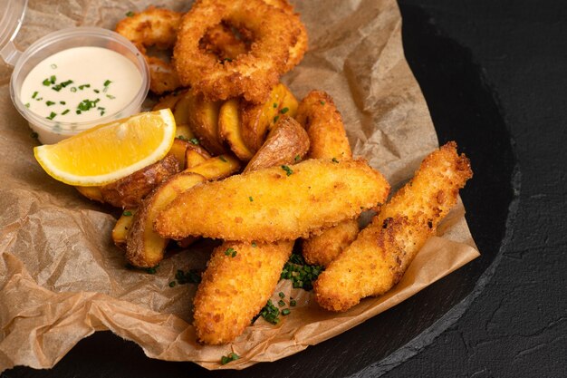 Bier Snacks Tintenfischringe Käsesticks Pommes frites auf schwarzem Hintergrund Seitenansicht