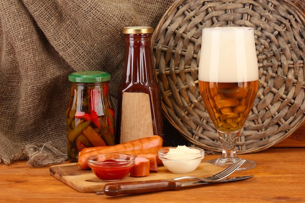 Bier und gegrillte Würste auf Holztisch auf Sackleinenhintergrund