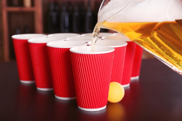 Bier wird in Plastikbecher auf den Tisch gegossen. Bier-Pong-Konzept