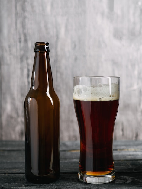 Bierflasche und Glas mit dunklem Lager auf hölzernem Hintergrund