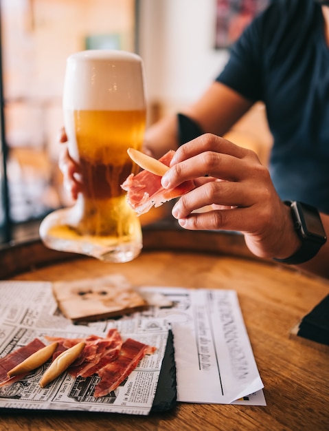 Bierglasstiefel mit köstlichen spanischen iberischen Schinkensnacks auf einem Holzfass