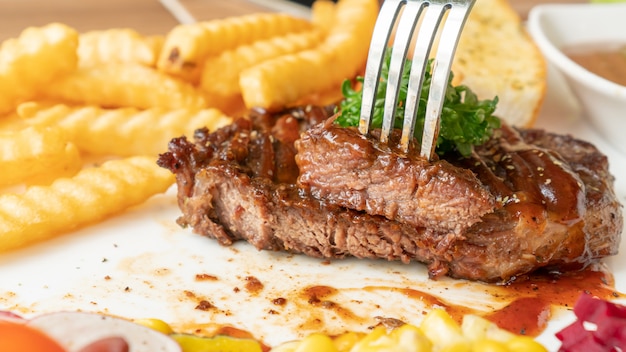 Bife, batatas fritas e vegetais em um prato branco.