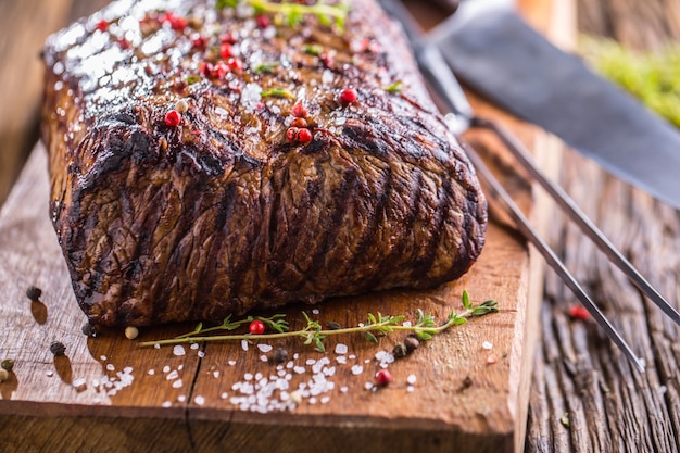 Bife. Bife de Rib Eye suculento na panela na placa de madeira com ervas e pimenta.