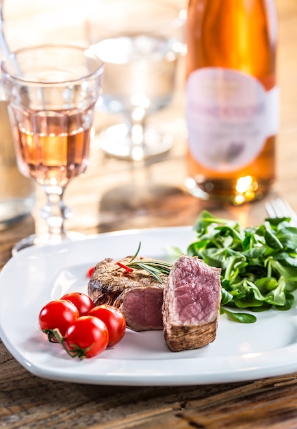 Bife. Bife suculento. Bife gourmet com legumes e copo de vinho rosé na mesa de madeira.