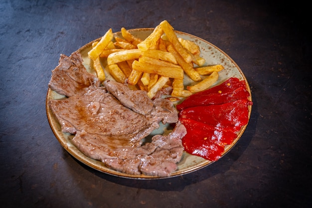 Bife com batata e pimentão vermelho em um fundo preto, em um prato branco