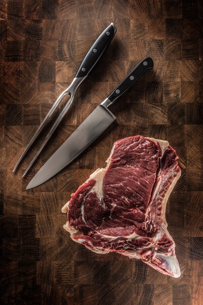 Bife de costilla con hueso sobre tabla de carnicero con tenedor y cuchillo.