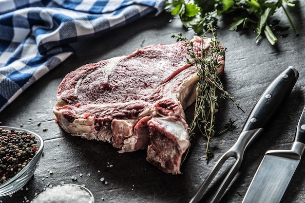 Bife de costilla con hueso sobre tablero de carnicero con hierbas sal pimienta tenedor y cuchillo.