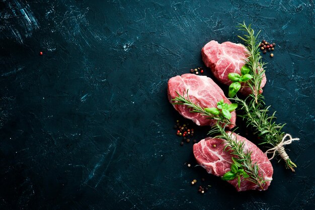 Bife cru. Carne com especiarias e ervas. Em um fundo de pedra preta. Vista do topo. Espaço de cópia grátis.