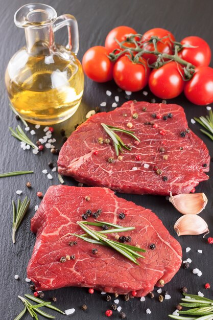 Bife cru com especiarias e ingredientes para cozinhar.