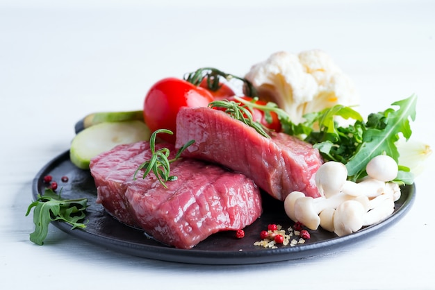 Bife cru no osso com legumes frescos em uma panela sobre um fundo branco, vista superior