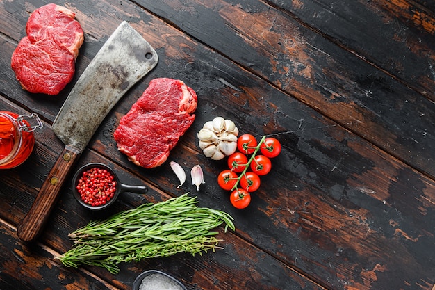 Bife de alcatra, bife de carne crua em mármore, com cutelo de faca de açougueiro velho e temperos na mesa rústica de madeira escura, vista superior com espaço para texto.