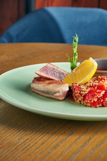 Bife de atum grelhado com enfeite de quinoa com tomate e molho vermelho em um prato na parede de madeira. Feche acima, foco seletivo