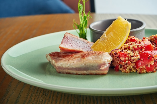 Bife de atum grelhado com enfeite de quinoa com tomate e molho vermelho em um prato na parede de madeira. Feche acima, foco seletivo