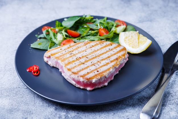 Bife de atum grelhado com legumes frescos, rúcula, espinafre e limão. Fechar-se.