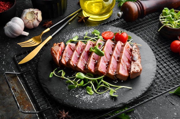 Bife de atum suculento cozido com legumes em uma placa de pedra preta Comida de restaurante Frutos do mar Estilo rústico Flat Lay