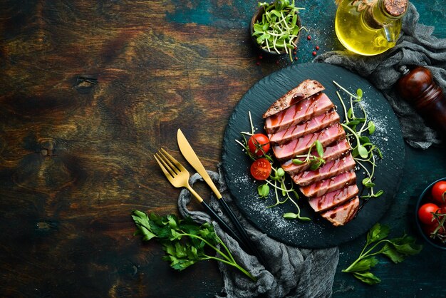 Bife de atum suculento cozido com legumes em uma placa de pedra preta Comida de restaurante Frutos do mar Estilo rústico Flat Lay