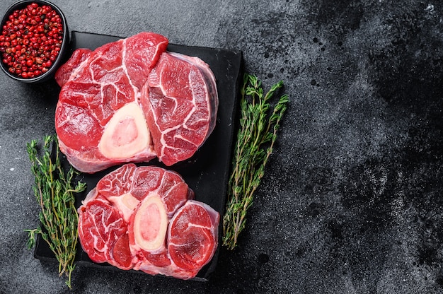 Bife de carne bovina crua Bife de osso buco pernil, ossobuco italiano. Fundo preto. Vista do topo. Copie o espaço.