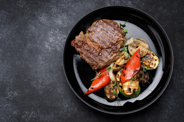 Bife de carne com legumes grelhados em uma placa preta