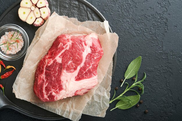 Bife de carne crua Bife de mandril fresco cru com sal de alecrim e pimenta na tábua sobre fundo escuro de concreto Bife de carne crua e especiarias para cozinhar