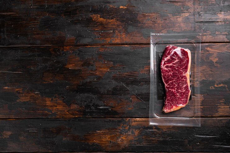 Foto bife de carne crua de nova york é embalado em um conjunto de plástico, sobre fundo de mesa de madeira escura velha, vista superior plana, com espaço de cópia para texto