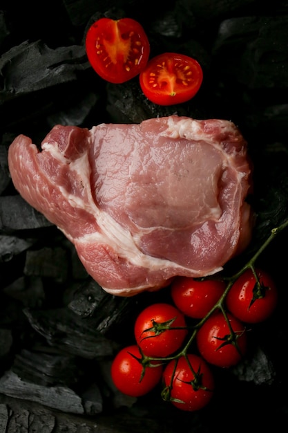 bife de carne crua em um fundo preto de bife cru de carvão com tomate cereja nas brasas