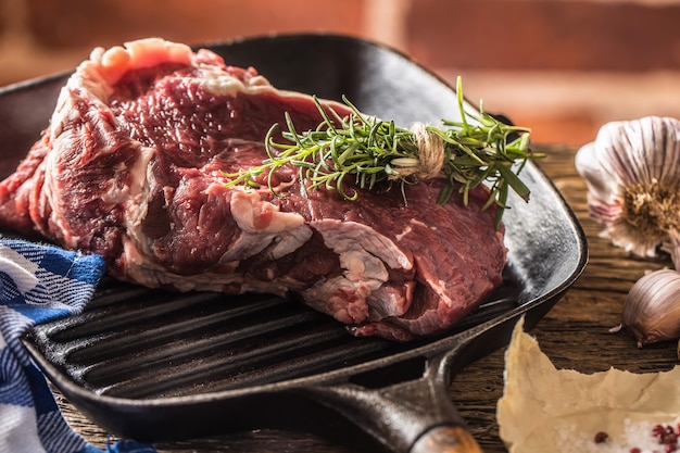 Bife de carne crua na assadeira com sal pimenta alho e ervas na mesa de madeira.