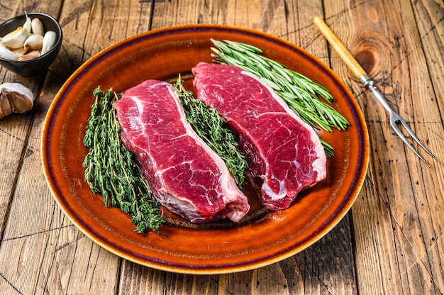 Bife de carne crua tira lombo em um prato com ervas. fundo de madeira. Vista do topo.