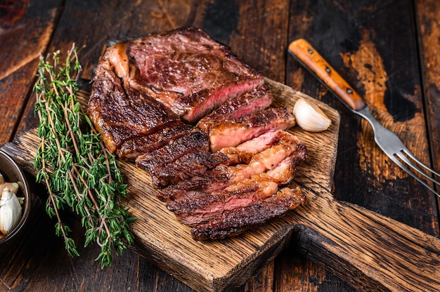 Bife de carne de bovino de olho de lombo assado e fatiado em uma tábua de madeira com tomilho na mesa de madeira. Vista do topo.