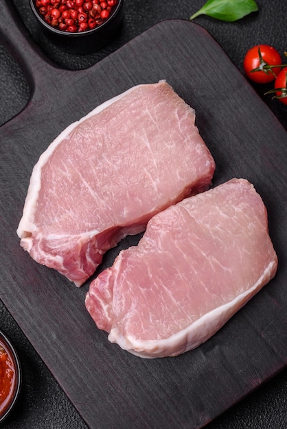 Bife de carne de porco fresca crua com especiarias salgadas e ervas numa tábua de madeira