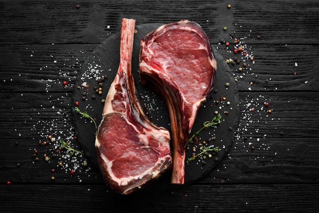 Bife de carne de tomahawk cru envelhecido seco com especiarias Em um fundo de madeira preto Vista superior Espaço para cópia grátis