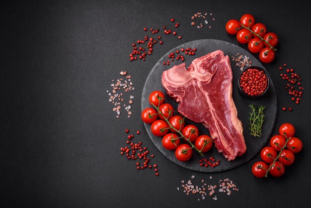 Bife de carne fresca crua e suculenta com especiarias de sal e ervas em um fundo escuro de concreto