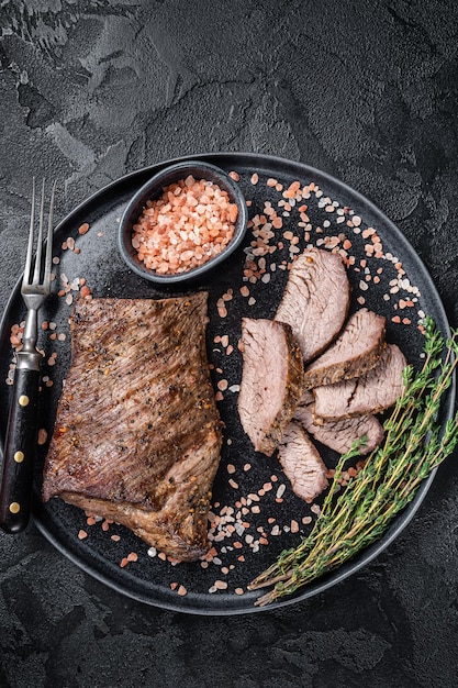 Bife de carne wagyu Tri Tip envelhecido para churrasco em um prato com sal rosa. Fundo preto. Vista do topo.