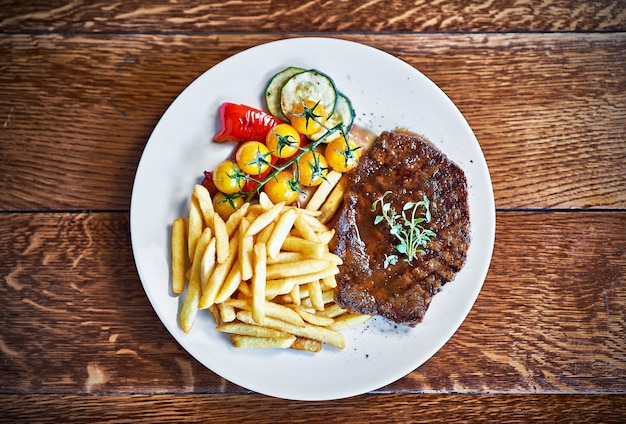 Bife de churrasco com batata frita servido em mesa de madeira