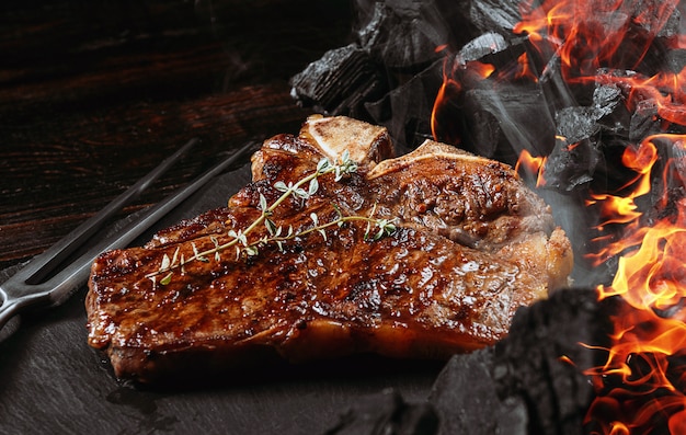 Foto bife de churrasco em uma placa de ardósia preta com garfo de carne e grelha de carvão