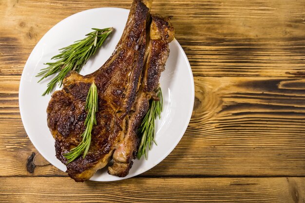 Bife de costela de carne assada no osso com alecrim em chapa branca na mesa de madeira