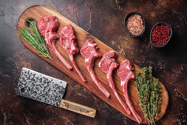 Bife de costeleta de cordeiro cru na tábua de açougueiro com alecrim e tomilho Fundo escuro Vista superior