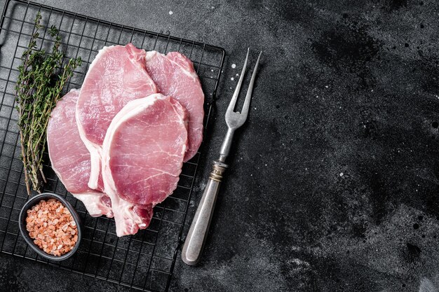 Bife de costeleta de porco cru para fritar na panela com ervas Fundo preto Vista superior Copiar espaço