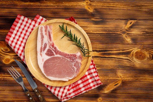 Bife de costeleta de porco crua na superfície de madeira escura.