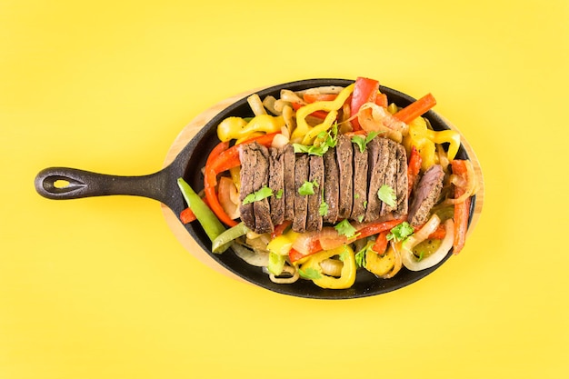 Bife de fajitas com pimentão e cebola amarela em uma frigideira de fajita de ferro fundido.