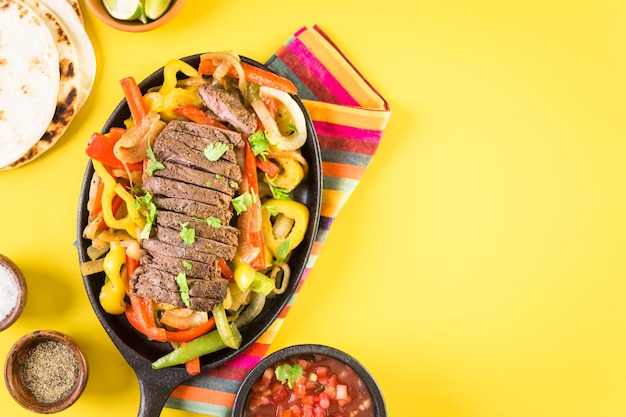 Bife de fajitas com pimentão e cebola amarela em uma frigideira de fajita de ferro fundido.