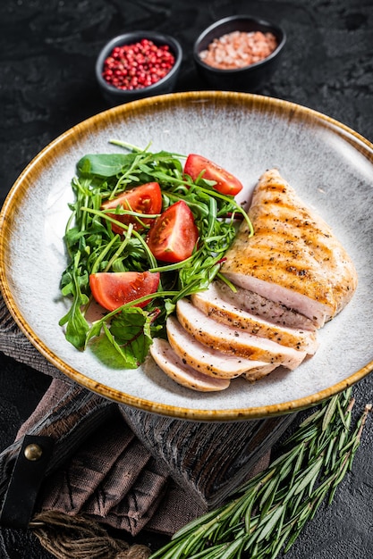 Bife de filé de peito de frango fatiado com salada verde em um prato Fundo preto Vista superior