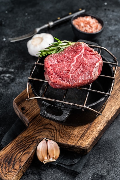 Bife de filé mignon cru em uma grelha com ervas. Fundo preto. Vista do topo.