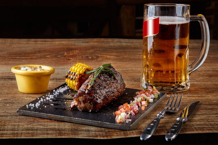 Foto bife de filé mignon grelhado e molho de cogumelos na tábua de corte preta e copo de cerveja no w ...