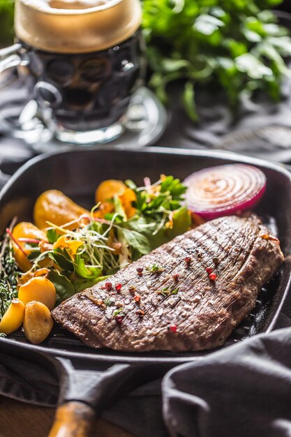 Foto bife de flanco de carne na frigideira com batata, puré, decoração de erva de alho e cerveja.