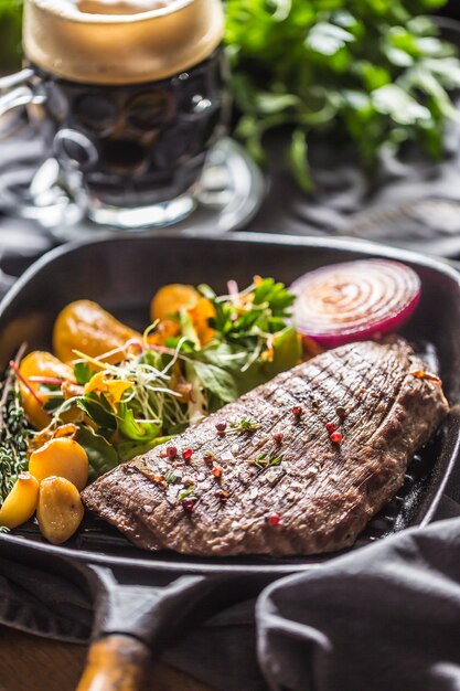 Bife de flanco na assadeira grelhada com decoração de ervas de purê de batata e alho e chope.