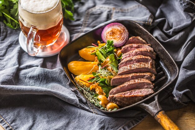 Bife de flanco na assadeira grelhada com decoração de ervas de purê de batata e alho e chope.